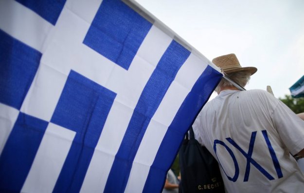 epa04829932 A man wearing an 'OXI' (No) T-shirt holds a Greek national flag during a demonstration in Berlin, Germany 03 July 2015, gathering supporters of the 'No' voting in the Greek referendum to be held on 05 July. The rally of several hundred demonstrators was held under the theme 'Nein!Oxi!No! to austerity - Yes to democracy.'  EPA/KAY NIETFELD